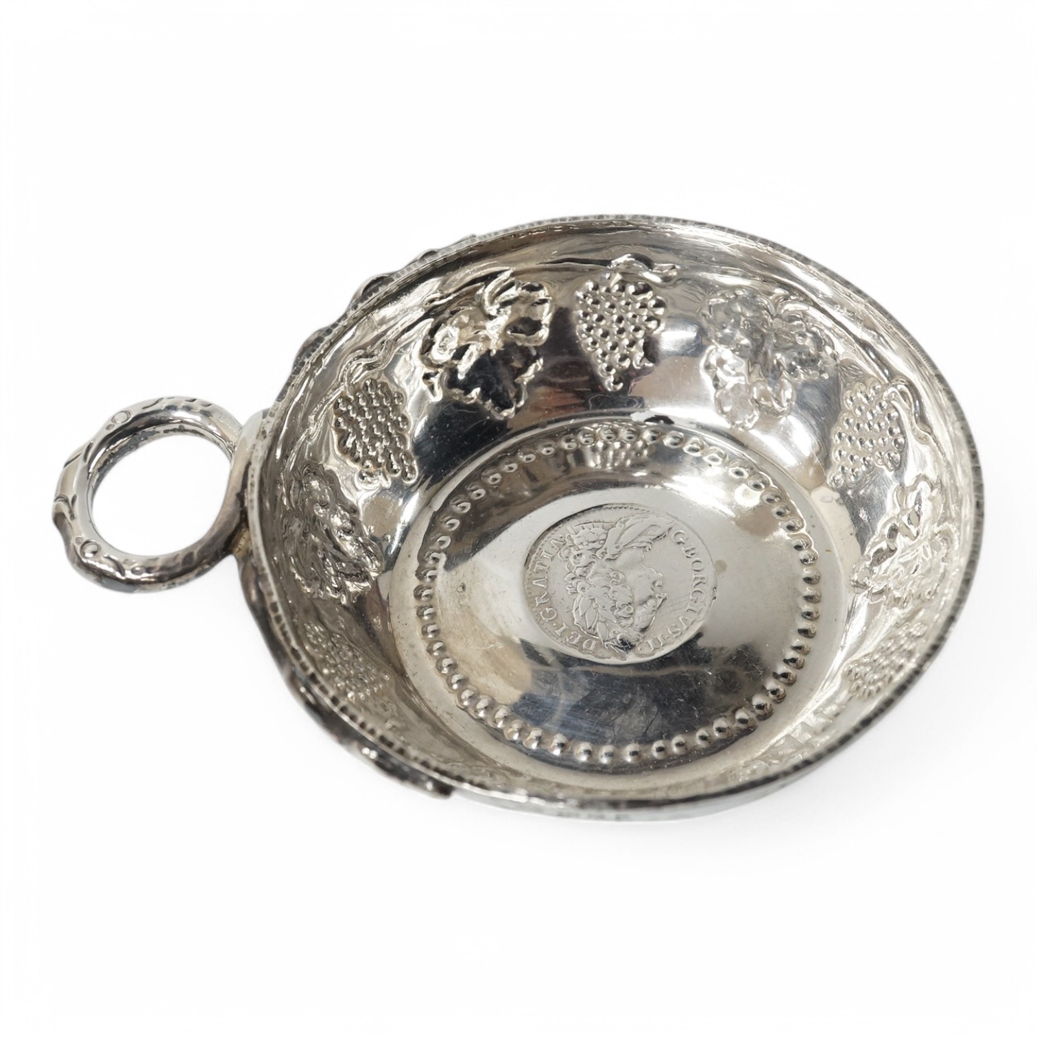 A George V silver taste vin, by Daniel & John Welby, with fruiting vine decoration and inset coin centre, London, 1924, diameter 92mm, 4.1oz. Condition - fair to good